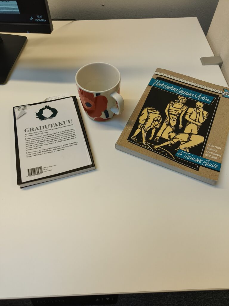 Kuva työpöydän reunalta, jossa on kahvikuppi ja kaksi tutkimukseen liittyvää kirjaa.